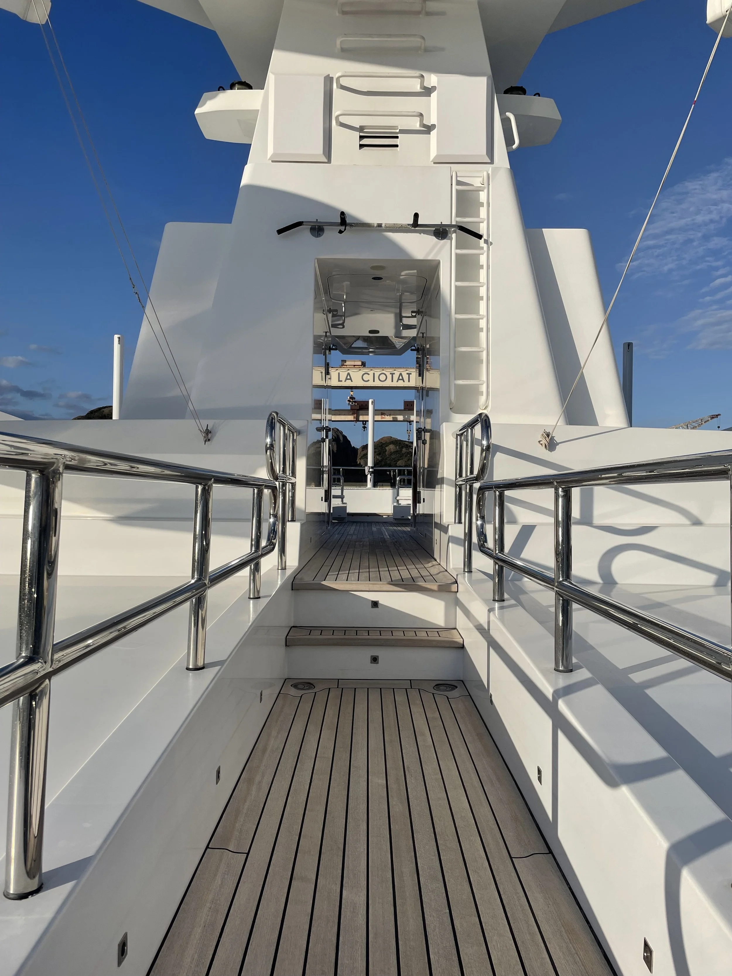 pont en bois sur un yacht blanc avec passerelle en acier inoxydable et vue vers le ciel bleu avec nuages avec grue de la Ciotat historique