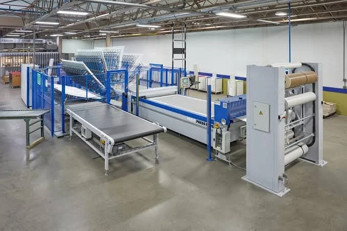 Industrial textile manufacturing machinery in a factory setting with multiple rollers and conveyor belts.