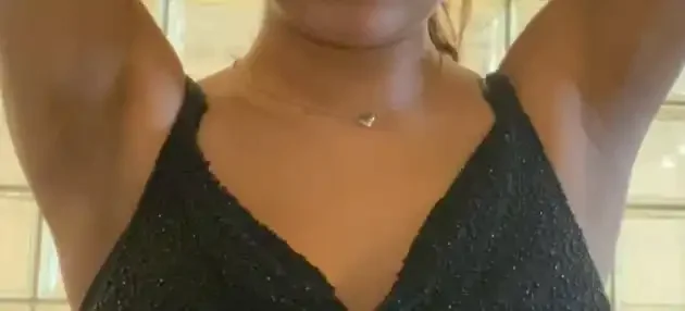 Close-up of a woman wearing a black, sparkly top with her arms raised.