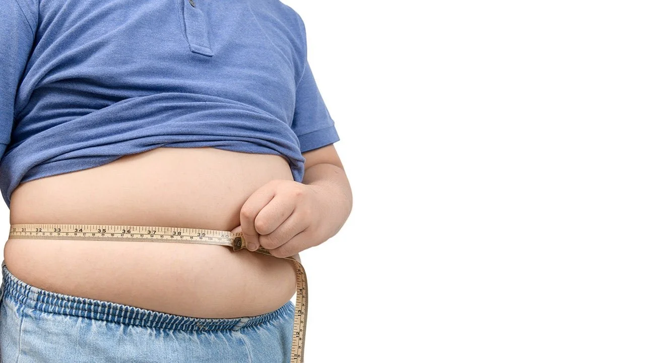 Person measuring their waist with a tape measure, wearing a blue t-shirt and light blue pants.
