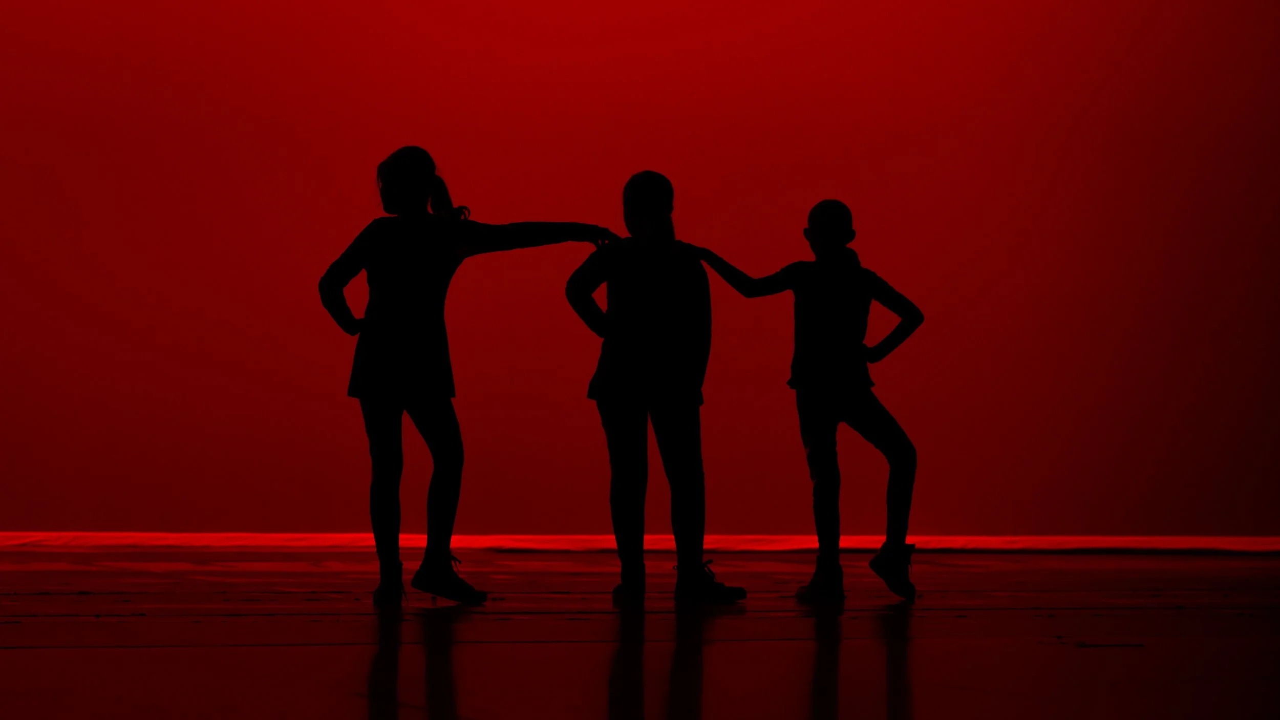 Silhouettes of three children standing together against a red background, with one child placing an arm on another's shoulder.