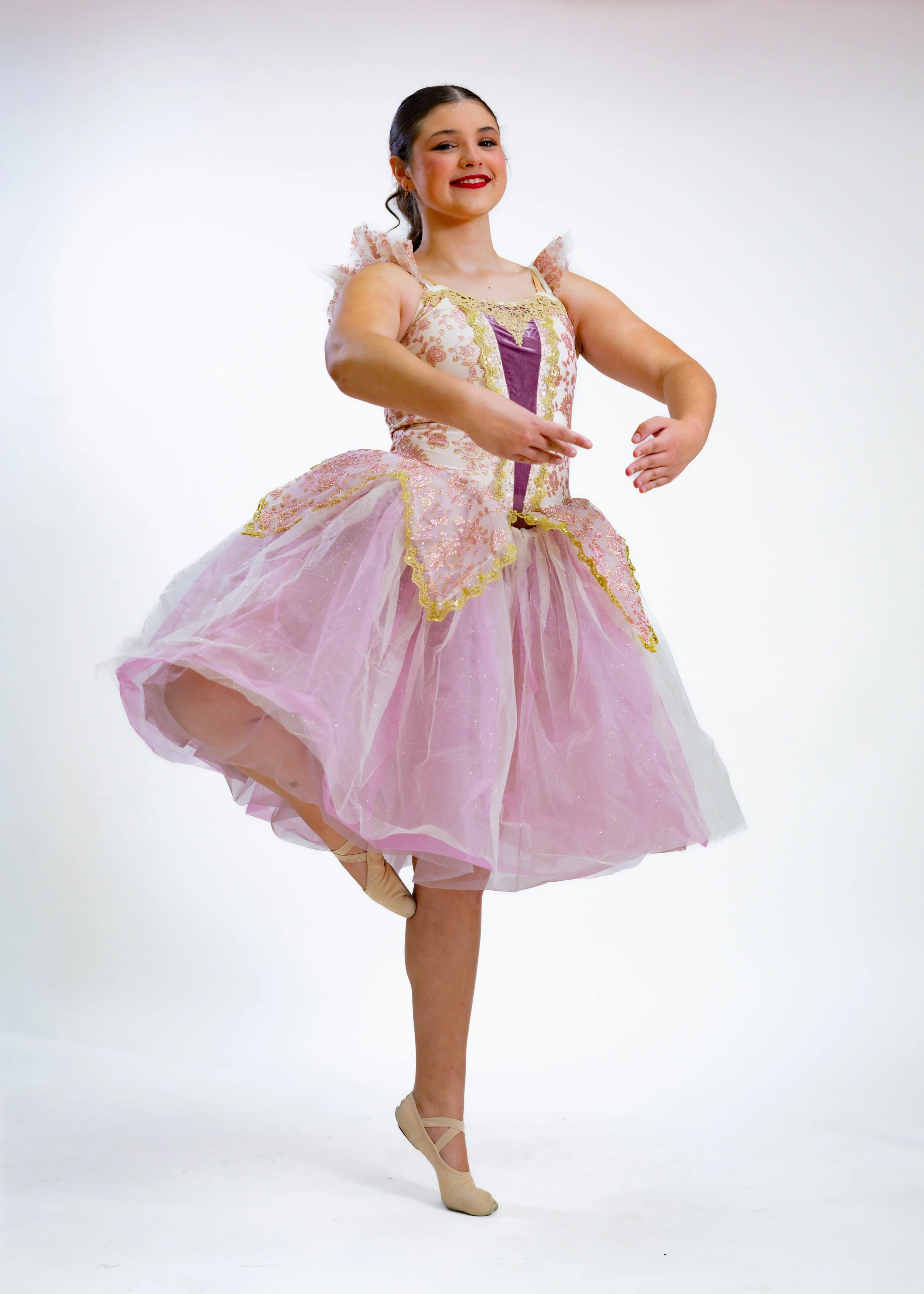 Ballet dancer in pink and purple tutu poses on one leg against a plain white background.