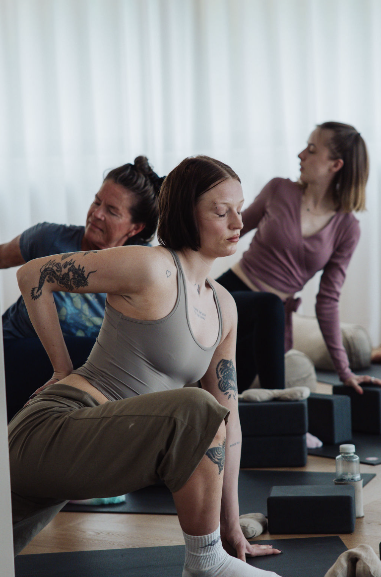 People practicing yoga in a studio, with a woman in the foreground performing a side stretch.