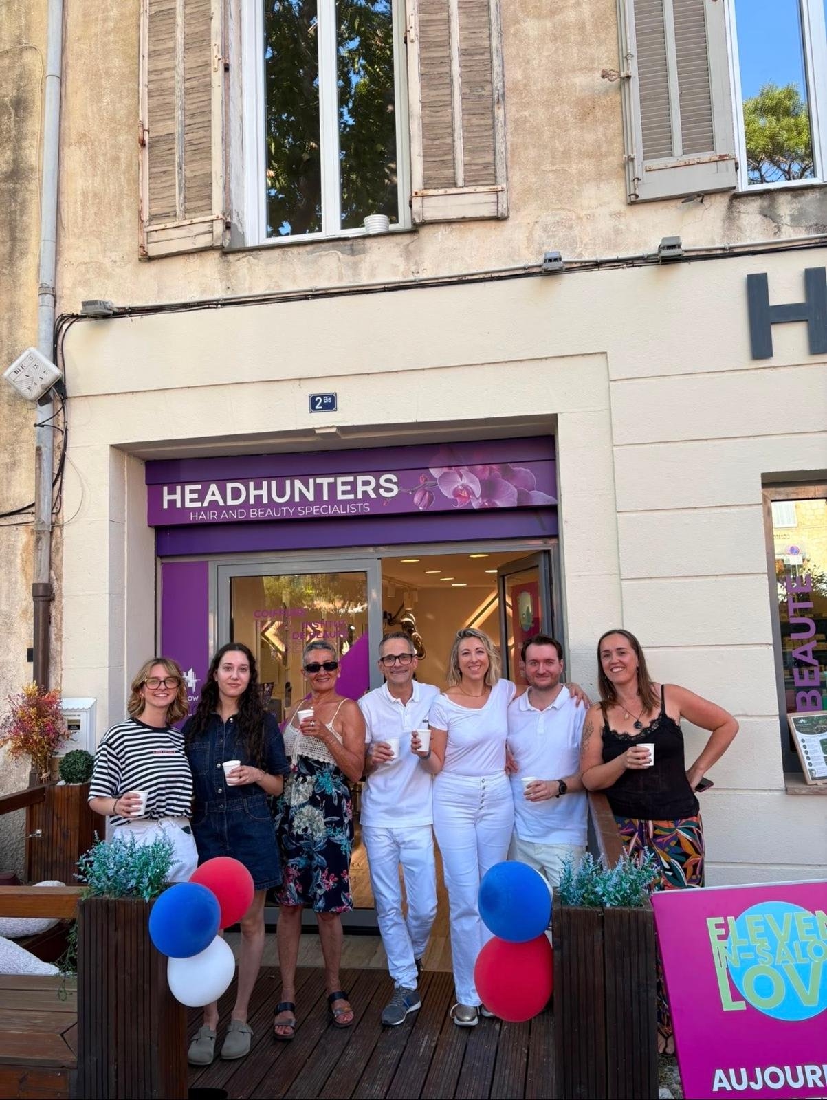 Groupe de sept personnes souriantes devant un salon de beauté nommé 'Headhunters'.