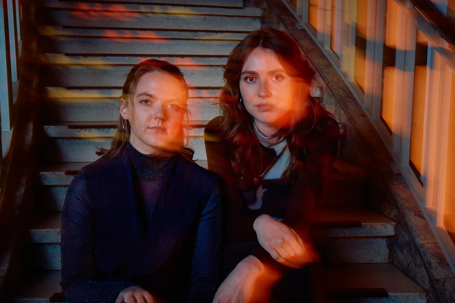 Two women sitting on stairs with orange light streaks across their faces.