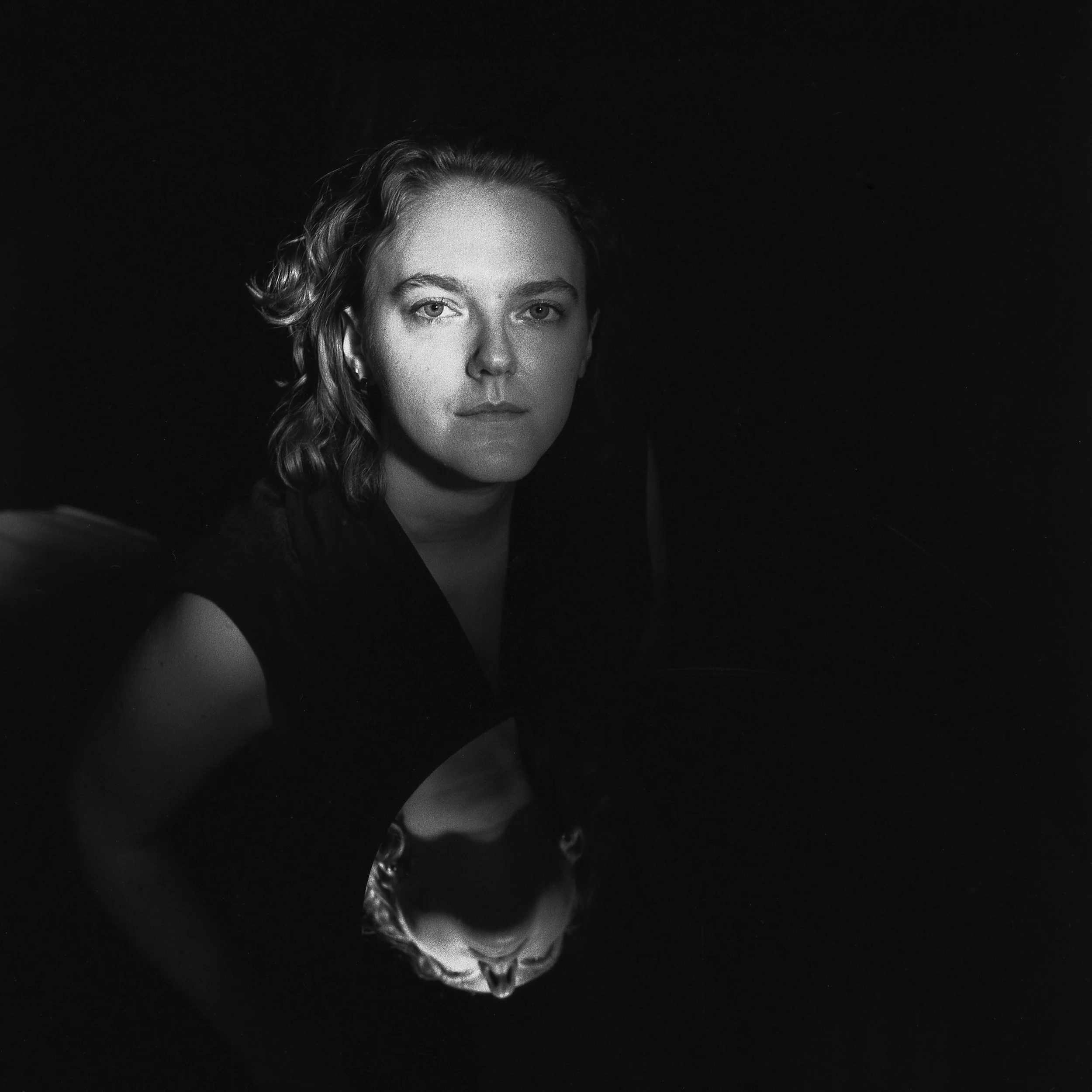 Black and white photo of a woman with wavy hair gazing at the camera, set against a dark background.