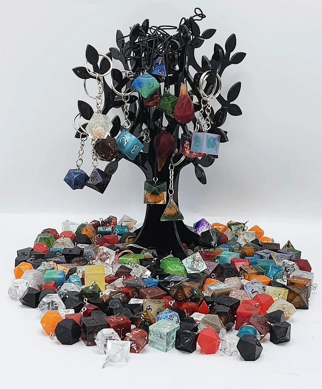 Photo depicting a multitude of anti-waste dice accessories at the bottom of a black colored tree display holding keychains and necklaces. The remaining dice accessories are mimicking ever expanding multicolored tree roots. In this picture you see a v