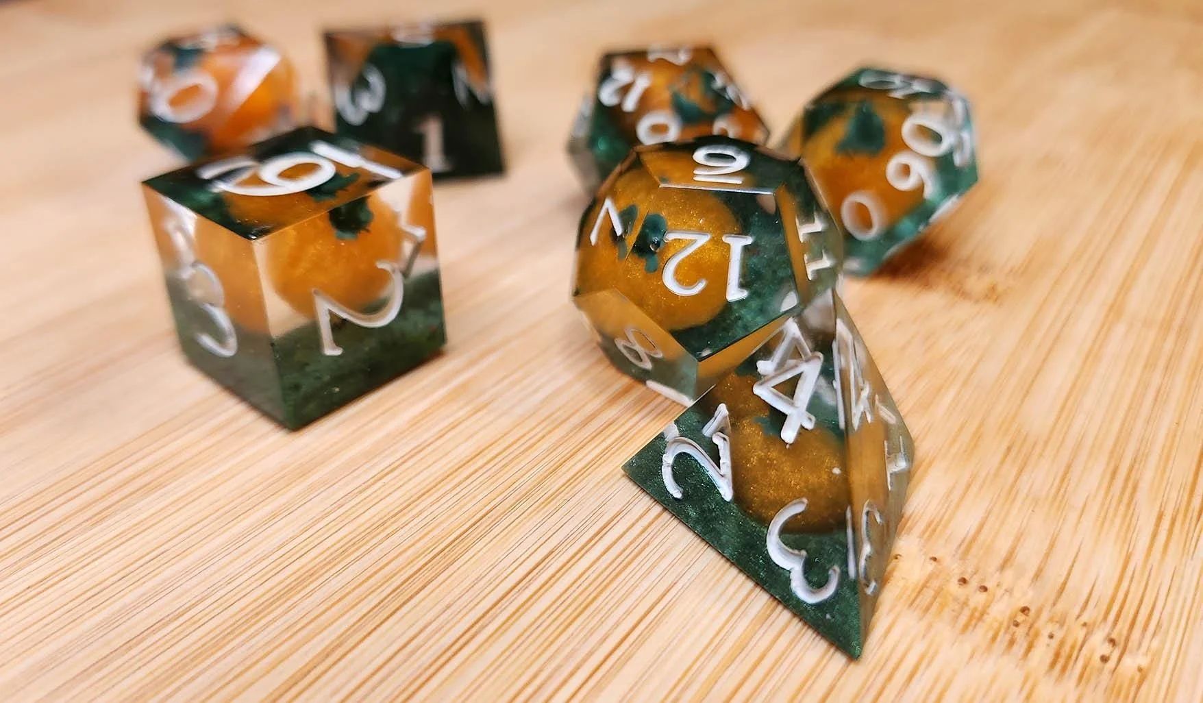 Close-up photo of JoaraCrafts' handmade clear resin DnD die featuring a tiny orange pumpkin inside with a green base focusing on the D4, D6 and D12. The polyhedral die is carefully crafted to showcase the miniature pumpkin from every angle, perfect f