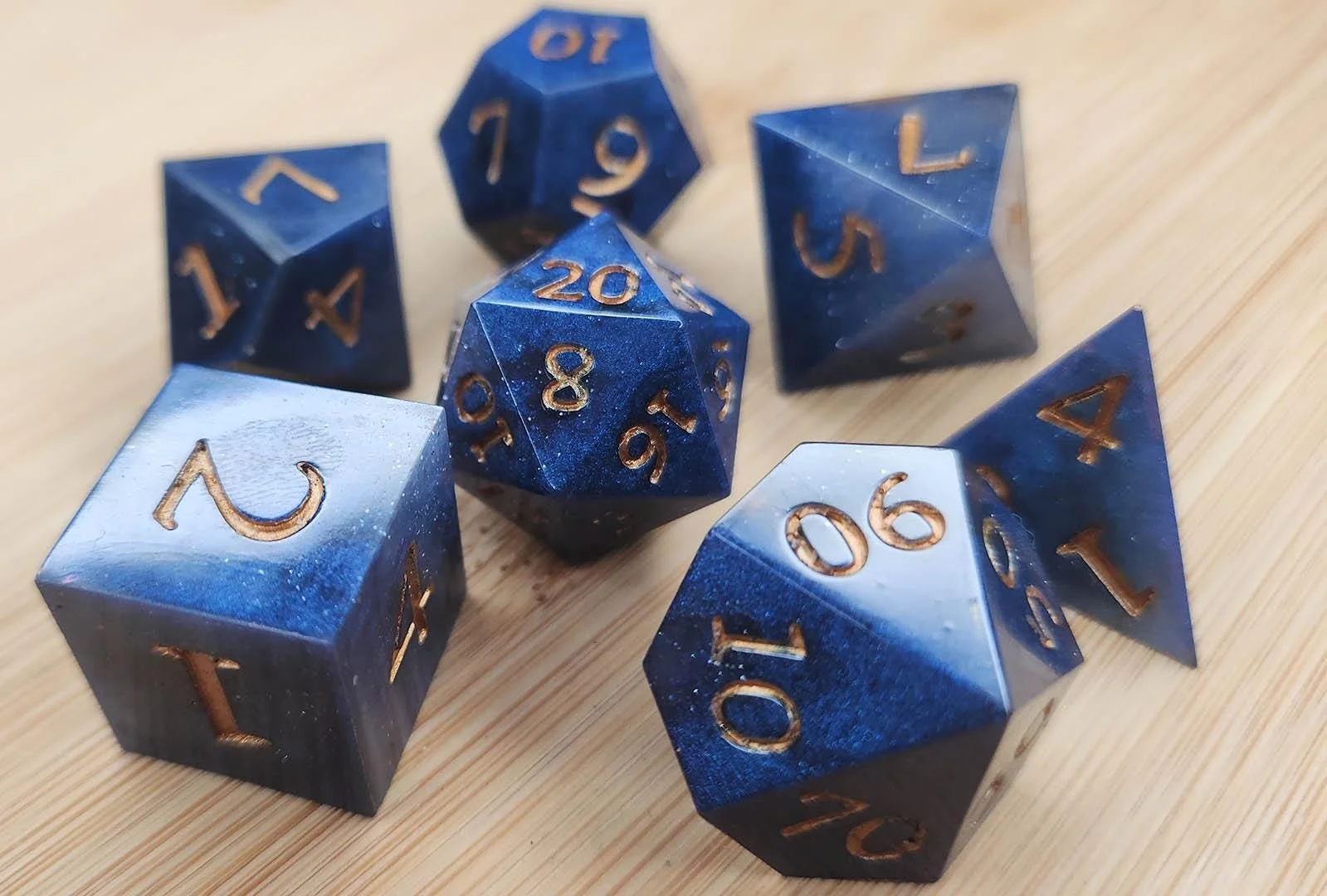 Detailed photo of the golden number variant of the Night Sky dnd dice sets. In this photo you can see how shiny the dice are and you can see the cloudy effect more clearly.