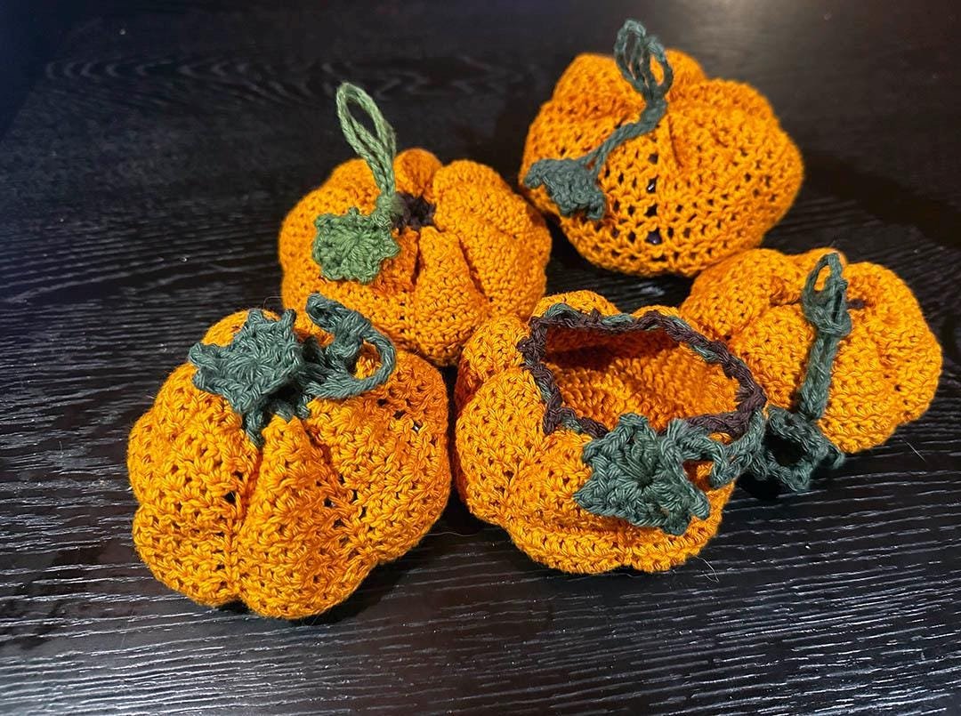 Five crocheted pumpkins in orange and green. The pumpkins are all different sizes and shapes.