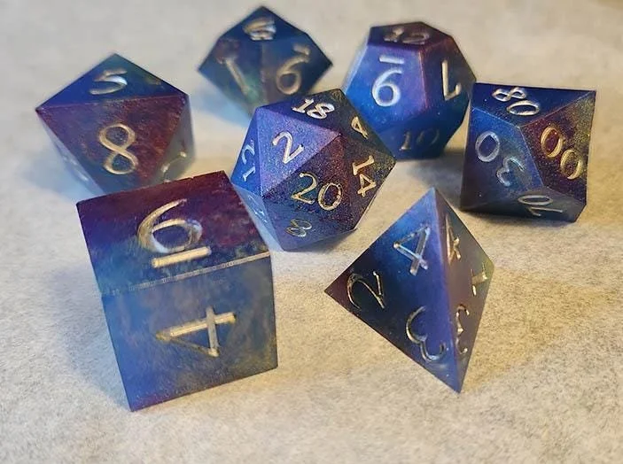 Detailed photo of JoaraCraft's Galaxy Lights dnd dice set focused on the D8, D6 and D20. The magenta and gold colors over the deep blue resin dice contrasting well with the silver numbers. All dice are handcrafted.