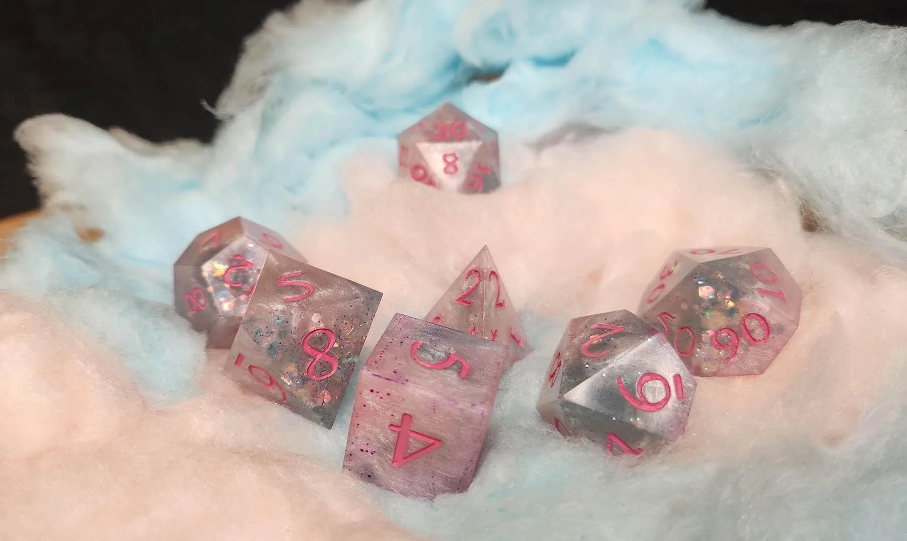 A detailed picture of the cotton candy dice on top of a pillow of pink and blue cotton candy. The bright pink numbers contrasting well with the rest of the background