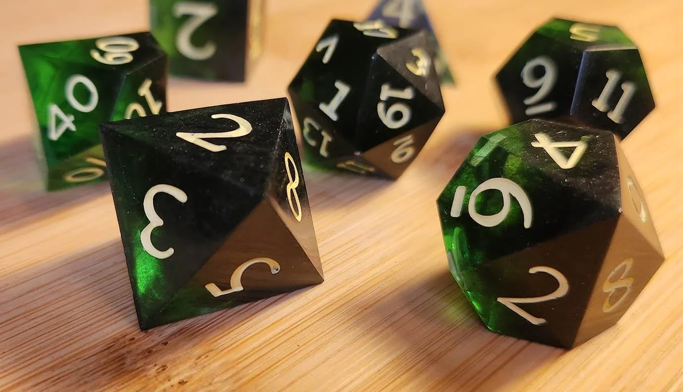 May include: A selection of polyhedral dice with a black and green marbled effect and yellow numerals. The dice are in various shapes and are displayed on a wooden surface, showing different faces and numbers.