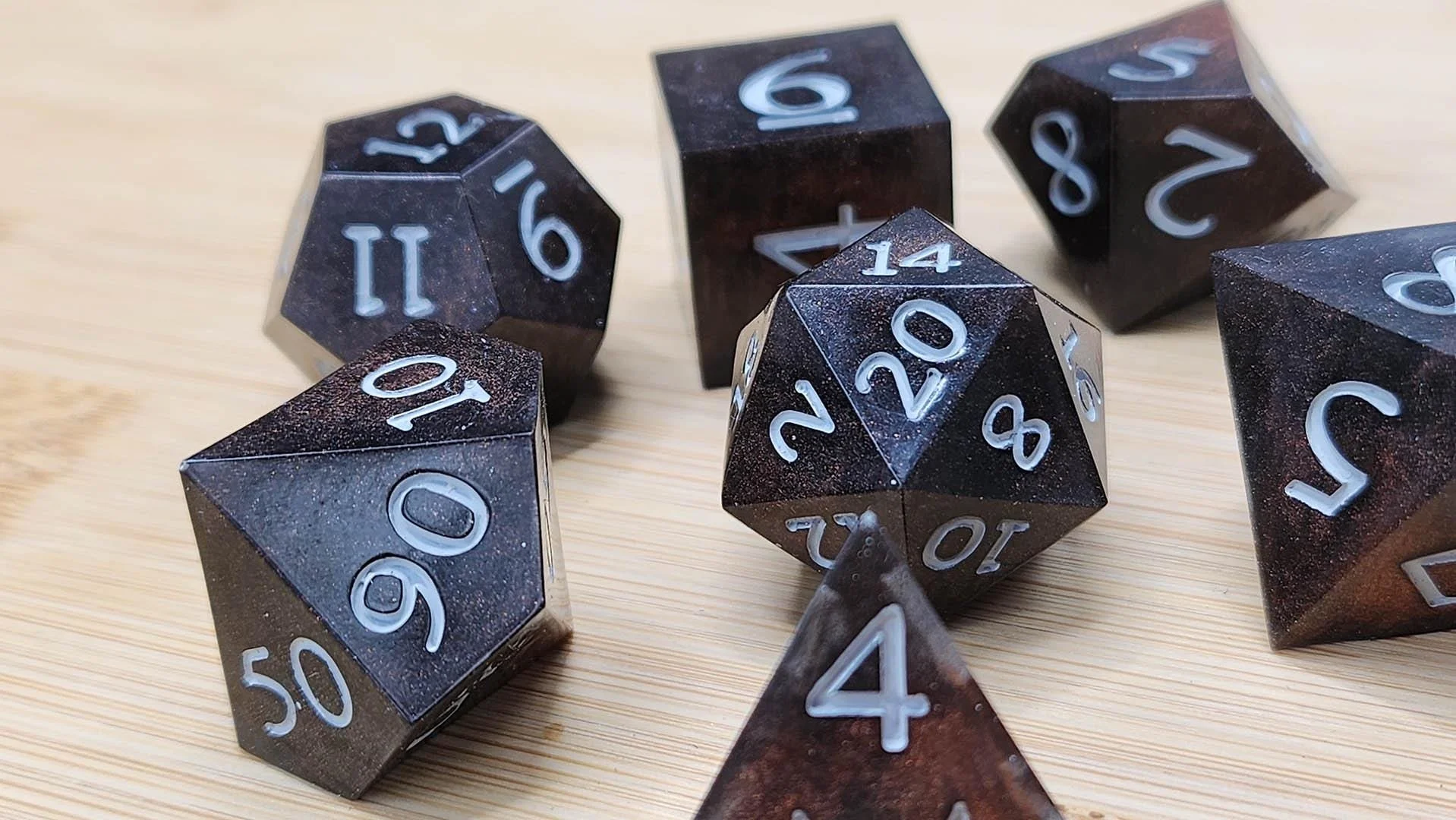 An impressive dark brown with lighter brown speckles dice set, the numbers are painted in white and the dice are displayed over a wooden surface