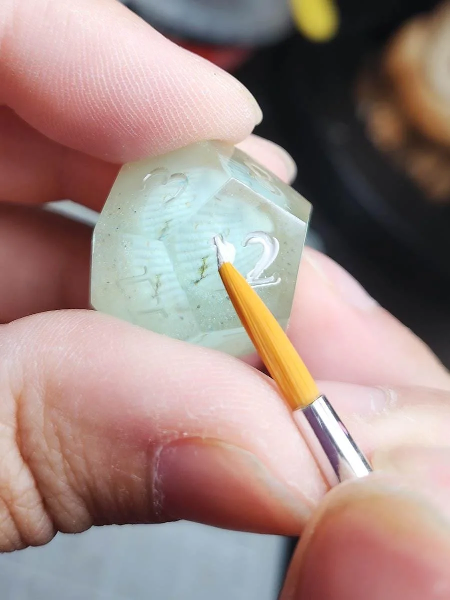 Joaracrafts Peaceful Ocean Dice Set for dungeons and dragons and other TTRPGs are a 7 piece dice set that mimic the appearance of real shells underwater. The dice are see-through blue and pale yellow with some sand to create a grainy effect, while th