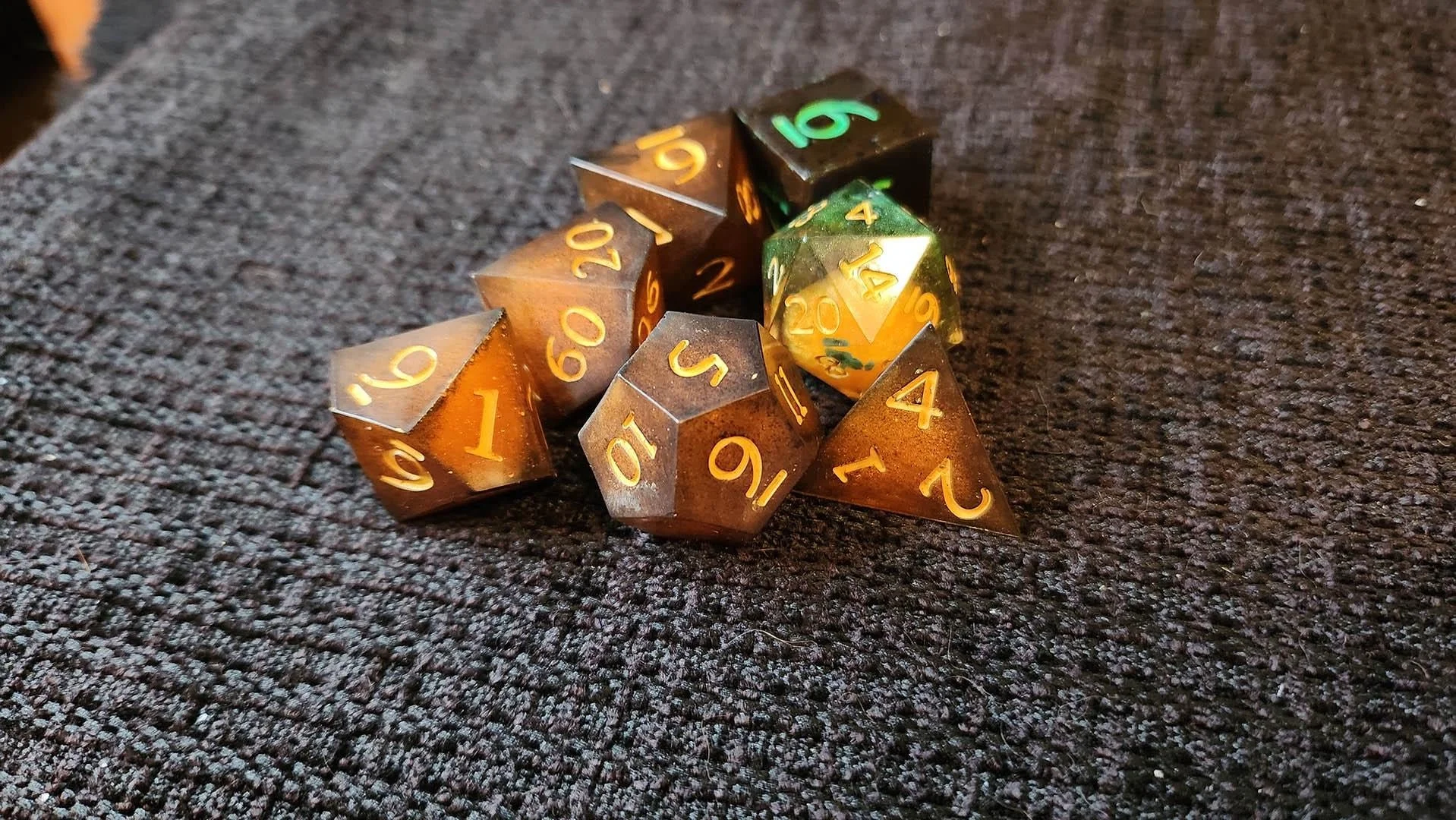 An example of how a JoaraCrafts mystery dice pack might look like. This specific set has a thematic orange and green variant where all dice have different shades of orange and some green details. One dice is darker dice with green numbers