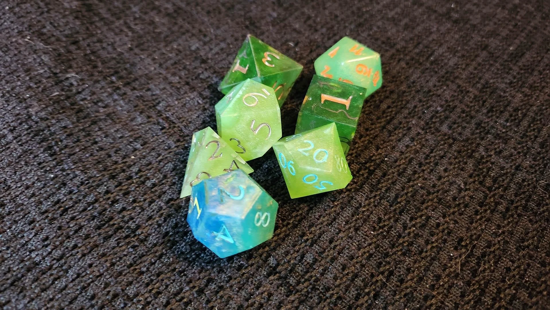 An example of how a JoaraCrafts mystery dice pack might look like. This specific set has a thematic green and blue variant where all dice have different shades of green and one blue dice with green numbers.