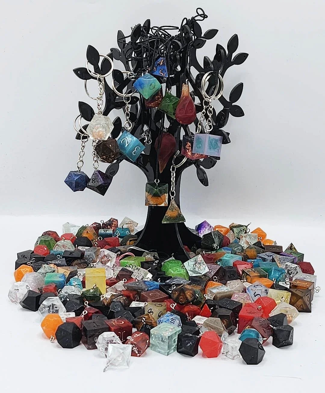 Photo depicting a multitude of anti-waste dice accessories at the bottom of a black colored tree display holding keychains and necklaces. The remaining dice accessories are mimicking ever expanding multicolored tree roots. In this picture you see a v