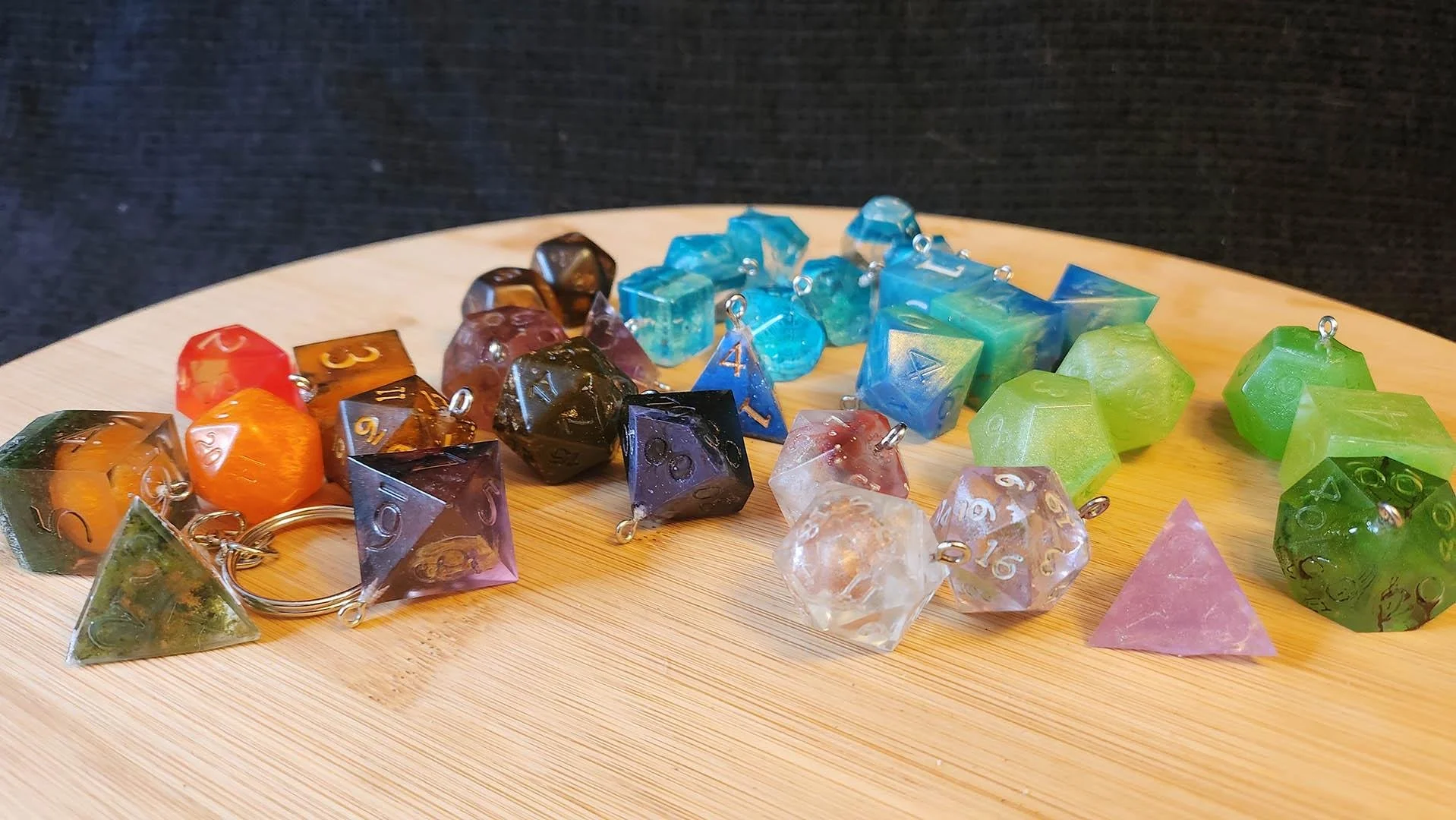 A photo with several types of Anti-Waste Dice Accessories from JoaraCrafts. From green, oranges, purples, clues, pinks, dark colors, bright colors or even transparent dice. There's a bit of everything on the wooden surface where all dice accessories 