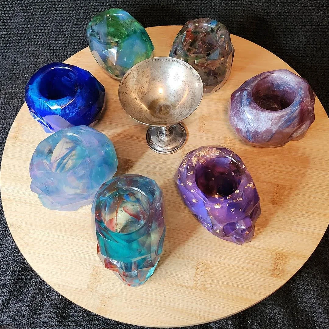 A photo of the JoaraCrafts Anti-Waste Resin Geometric Skull Pen Holder. In photo from above you can see several skulls in different colors and the slots for your stationary. The decorative skulls are displayed on a wooden circular base on a black clo
