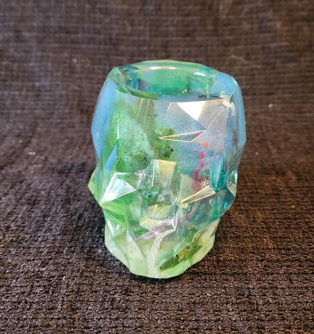 A detailed photo of one of the JoaraCrafts Anti-Waste Resin Geometric Skull Pen Holder. This skull is green and blue. The photo is taken with a black background.