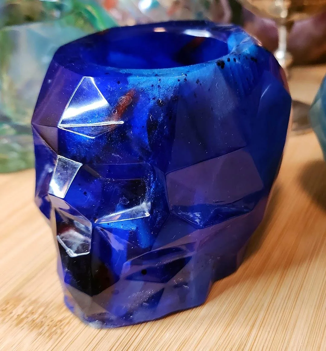 A detailed photo of one of the JoaraCrafts Anti-Waste Resin Geometric Skull Pen Holder. This skull is dark blue with brighter and darker chunks of resin on display. The photo is taken with a wooden background.