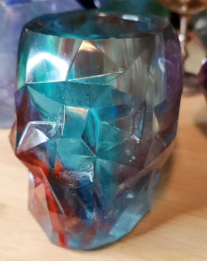 A detailed photo of one of the JoaraCrafts Anti-Waste Resin Geometric Skull Pen Holder. This skull is teal and with a red detail on the chin. The photo is taken with wooden background.