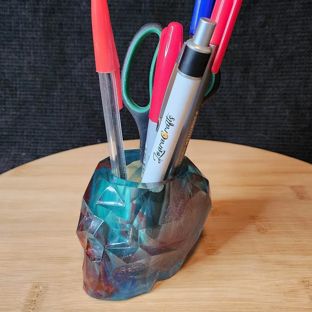 Colorful recycled resin anti-waste geometric skull desk organizer holding pens and scissors on a wooden surface.