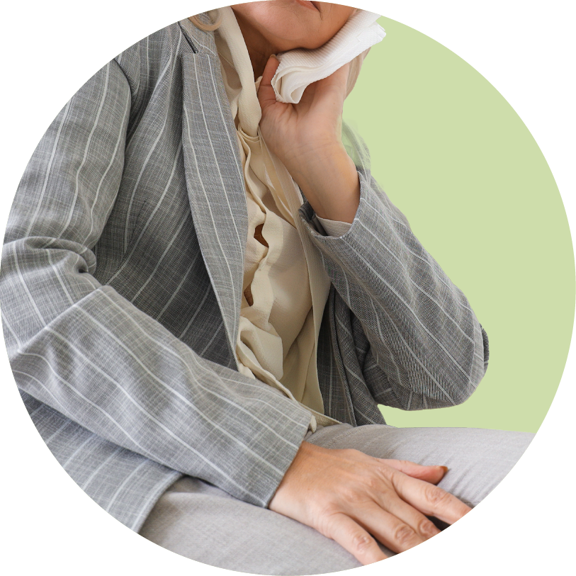 Person in a gray plaid suit sitting with a tissue to their nose, possibly indicating illness.