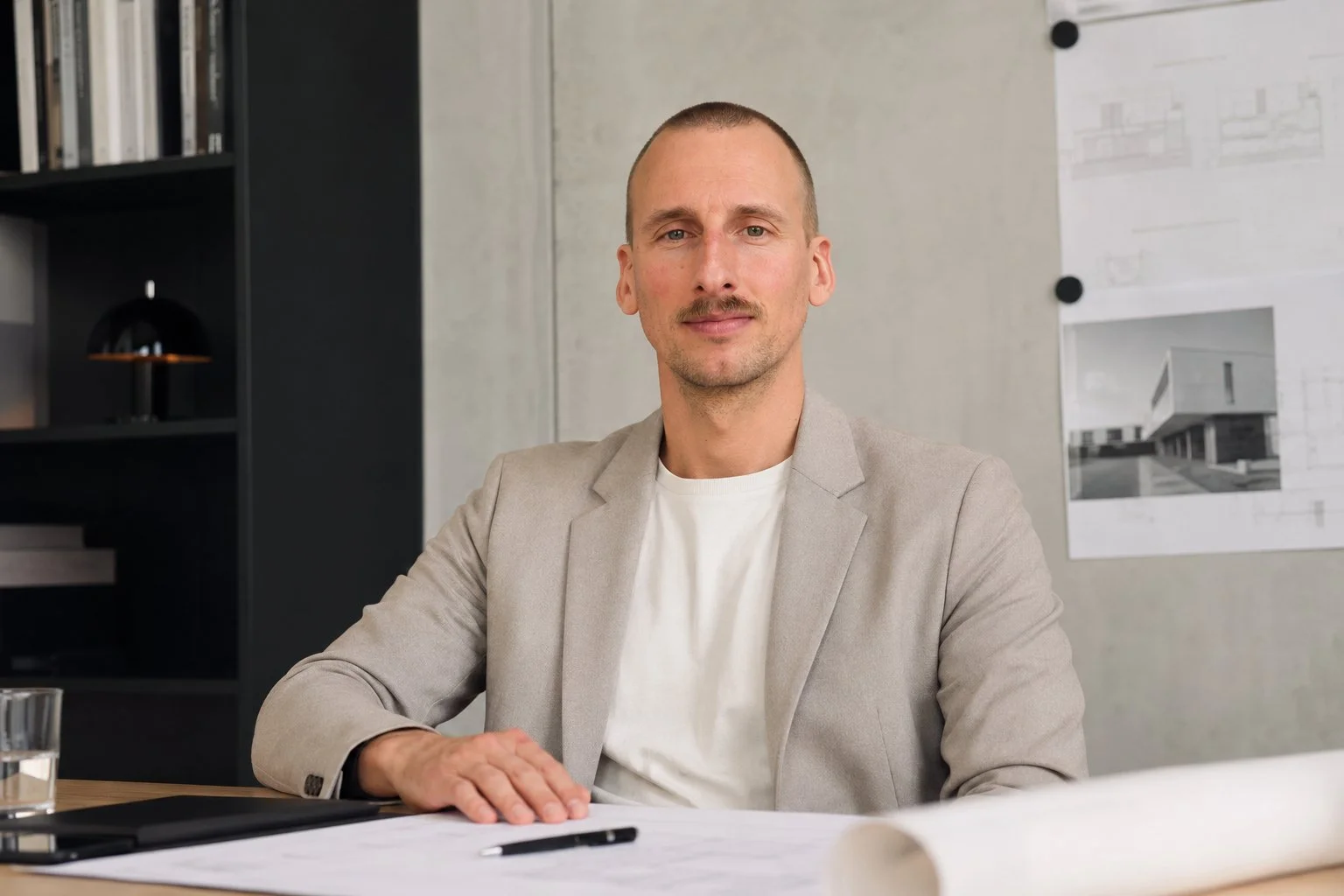 Adrian Lenz (Gründer und Geschäftsführer) sitzt am Tisch in einem Büro, trägt einen beigen Blazer und schaut in die Kamera.