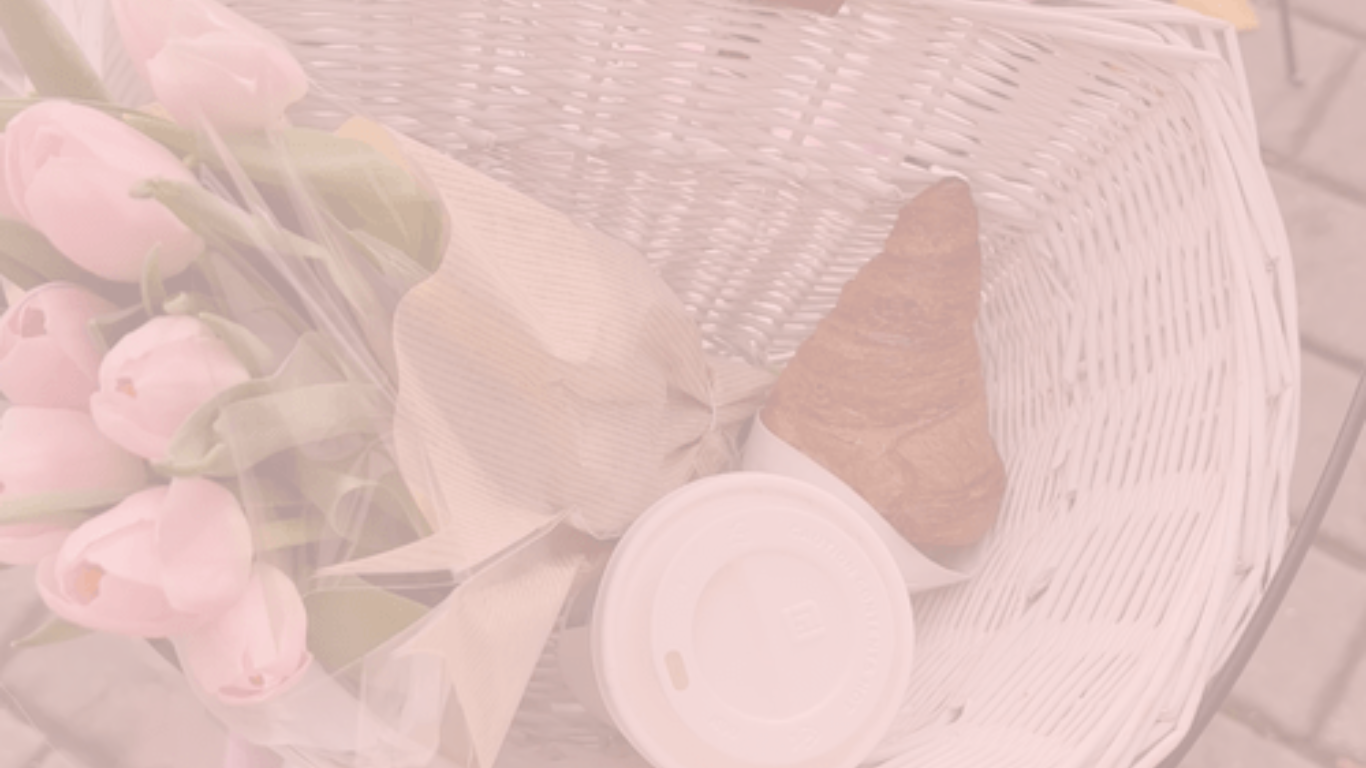 A pink flower bouquet wrapped in clear plastic, a wrapped croissant, and a white disposable coffee cup with a lid are placed on a white wicker chair.