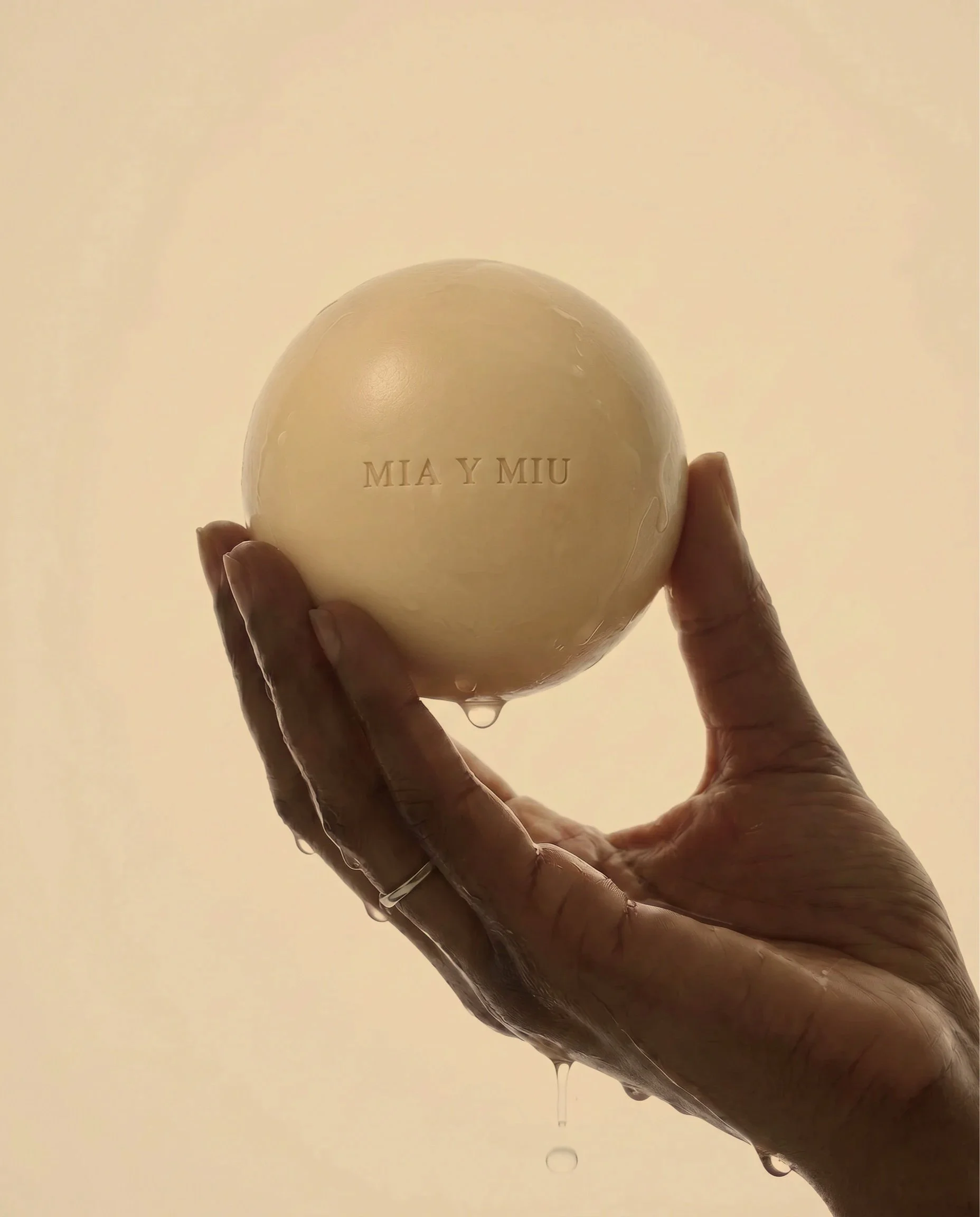 Mano sosteniendo una bola de jabón con gotas de agua y letras que dicen 'MIA Y MIU'