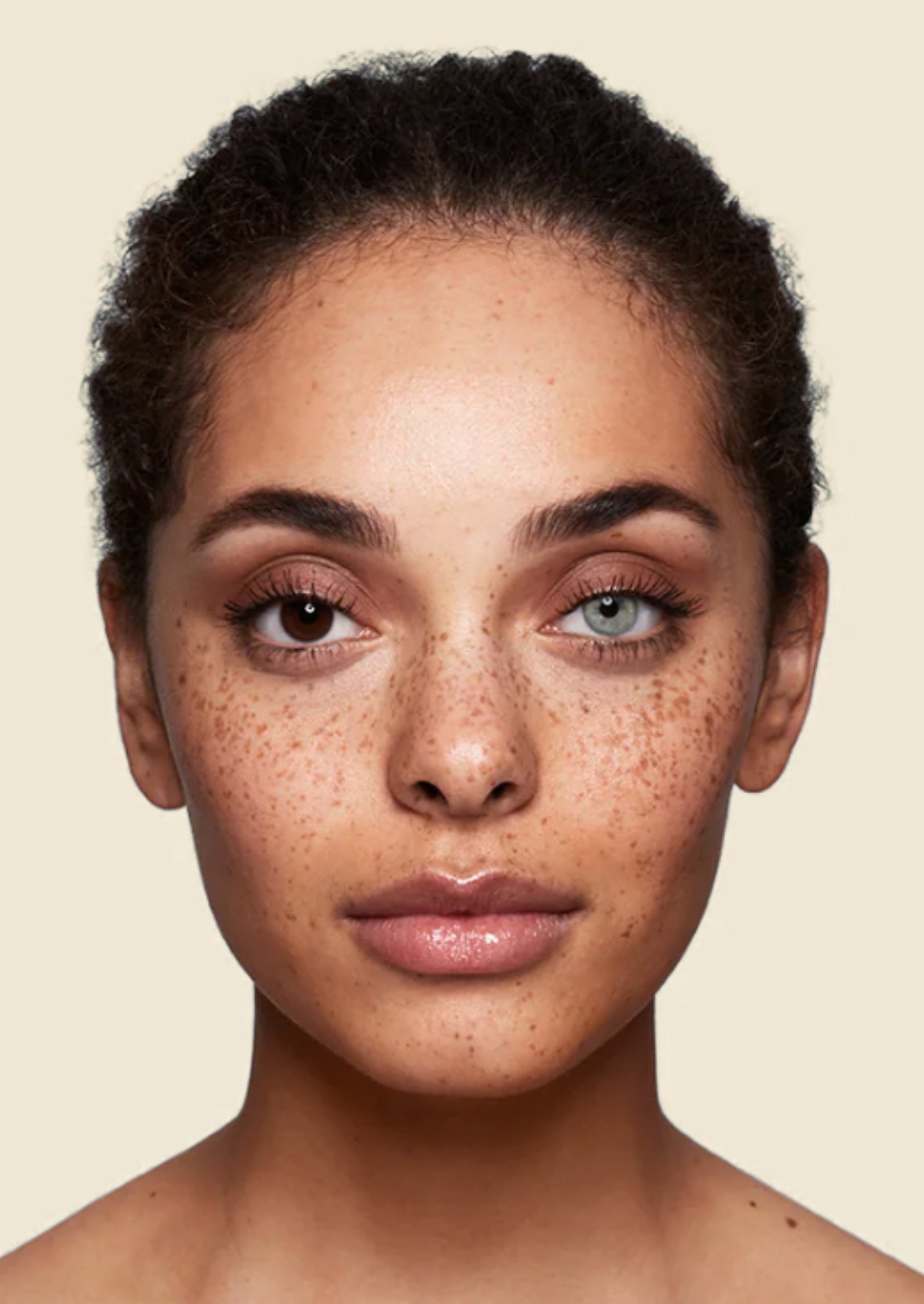 Retrato de una mujer con piel morena, ojos claros y cabello rizado y oscuro, mostrando solo la parte superior de su rostro y hombros.