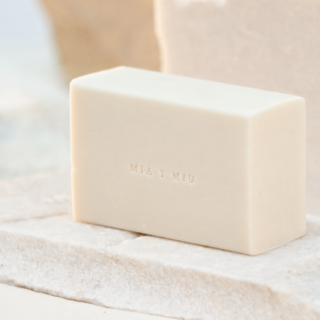 Jabón blanco con la marca 'MIA Y MIU' grabada en la parte frontal, sobre una superficie de piedra.