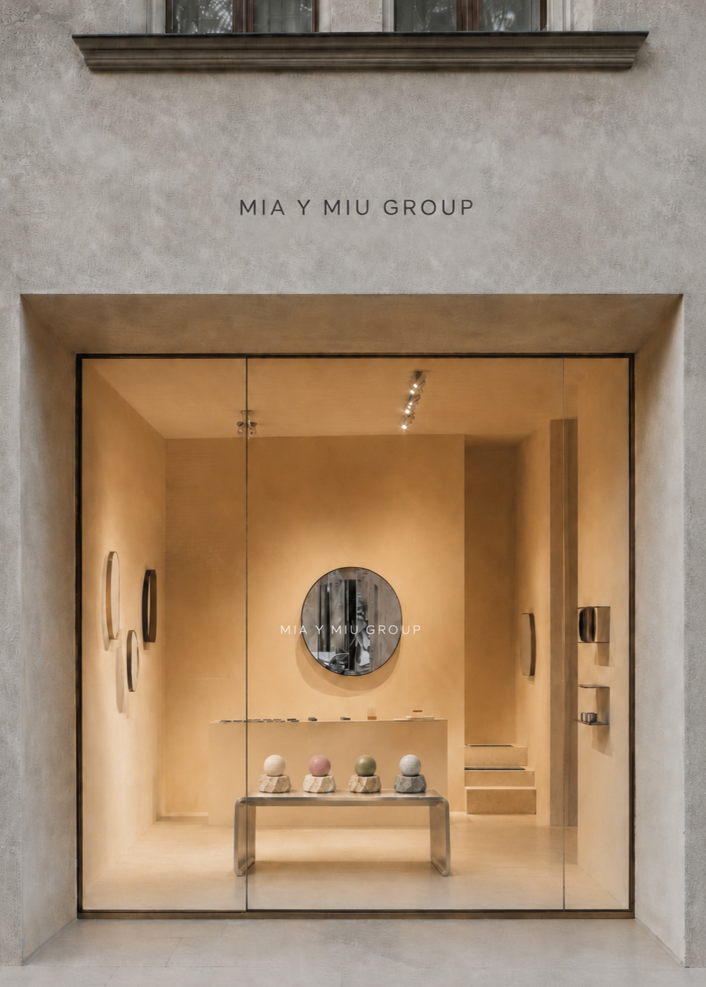 Vista frontal de la fachada de una tienda de la marca Mia y Miu Group, con un escaparate de vidrio que muestra objetos decorativos en tonos neutros y un espejo redondo en el fondo.