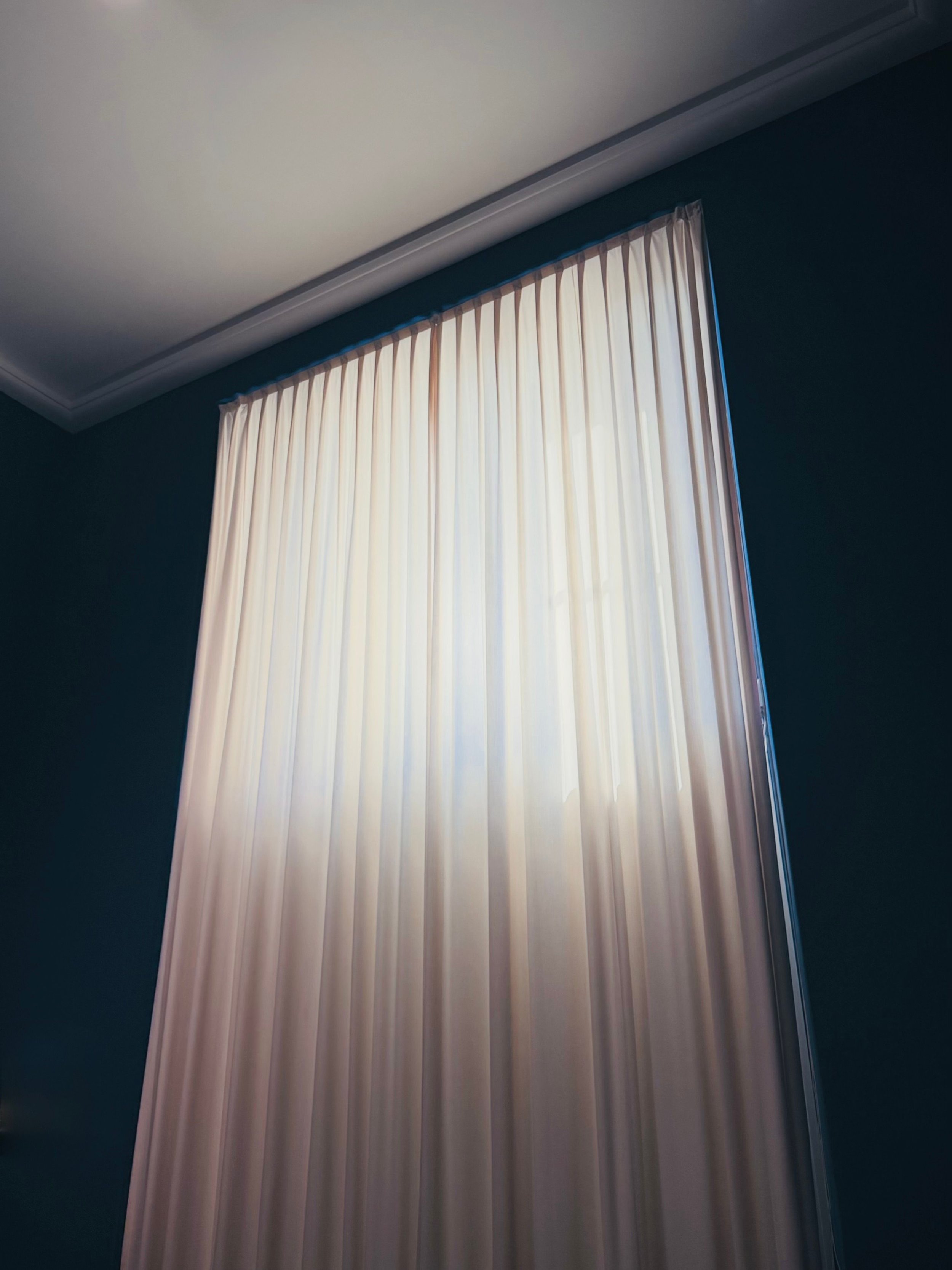 Cortinas blancas en una ventana en una habitación con paredes de color azul oscuro.