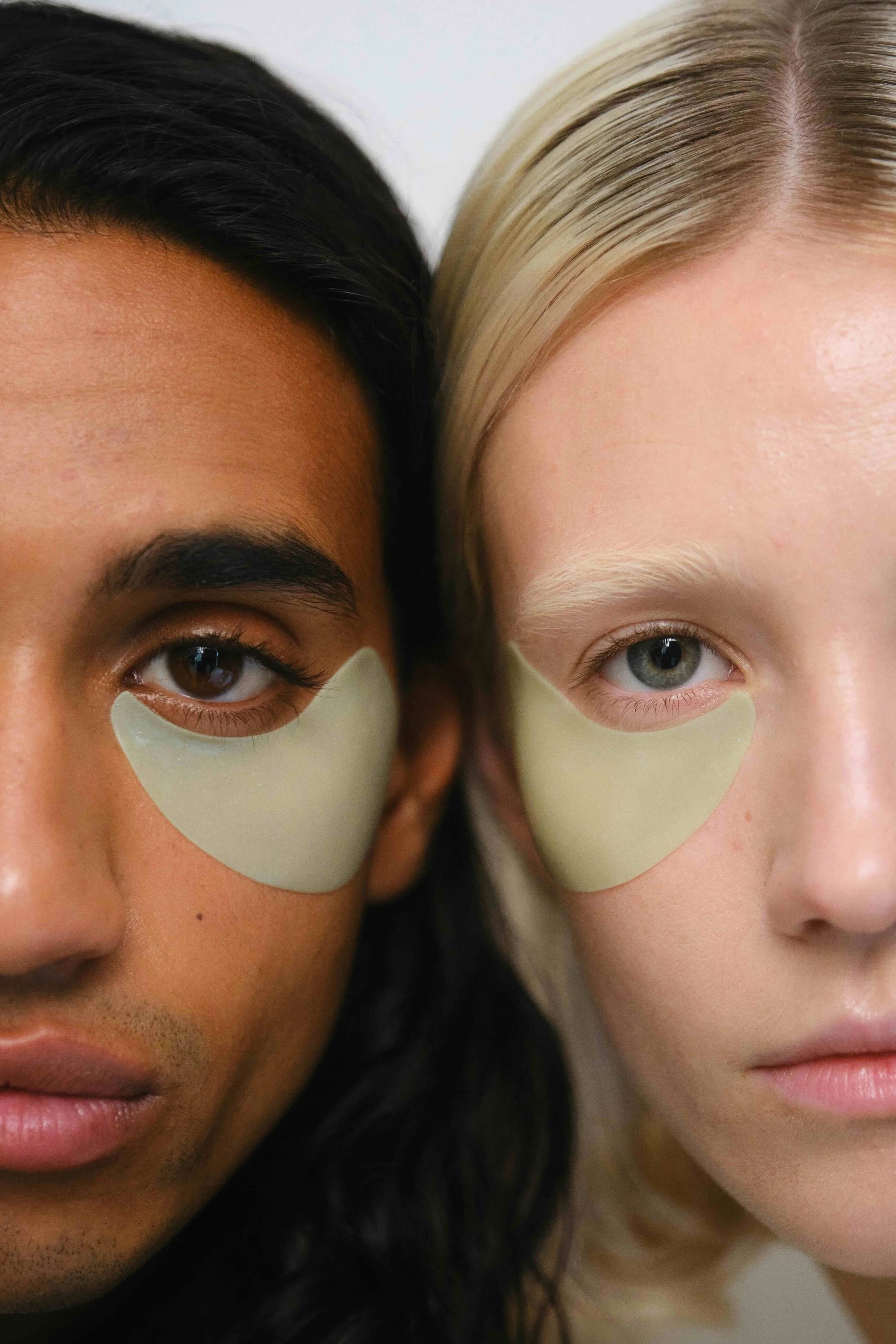 Primer plano de las caras de un hombre de piel morena y cabello oscuro, y una mujer de piel clara y cabello rubio, ambos con ingredientes faciales y con ojos abiertos.