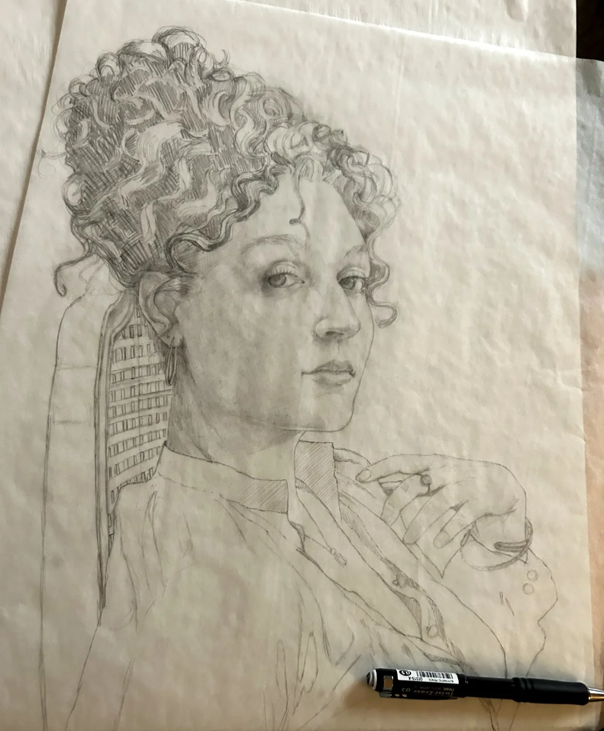 A detailed pencil sketch of a woman with curly hair, looking slightly to the side, with a hand resting near her chin. A pen is placed at the bottom of the paper.