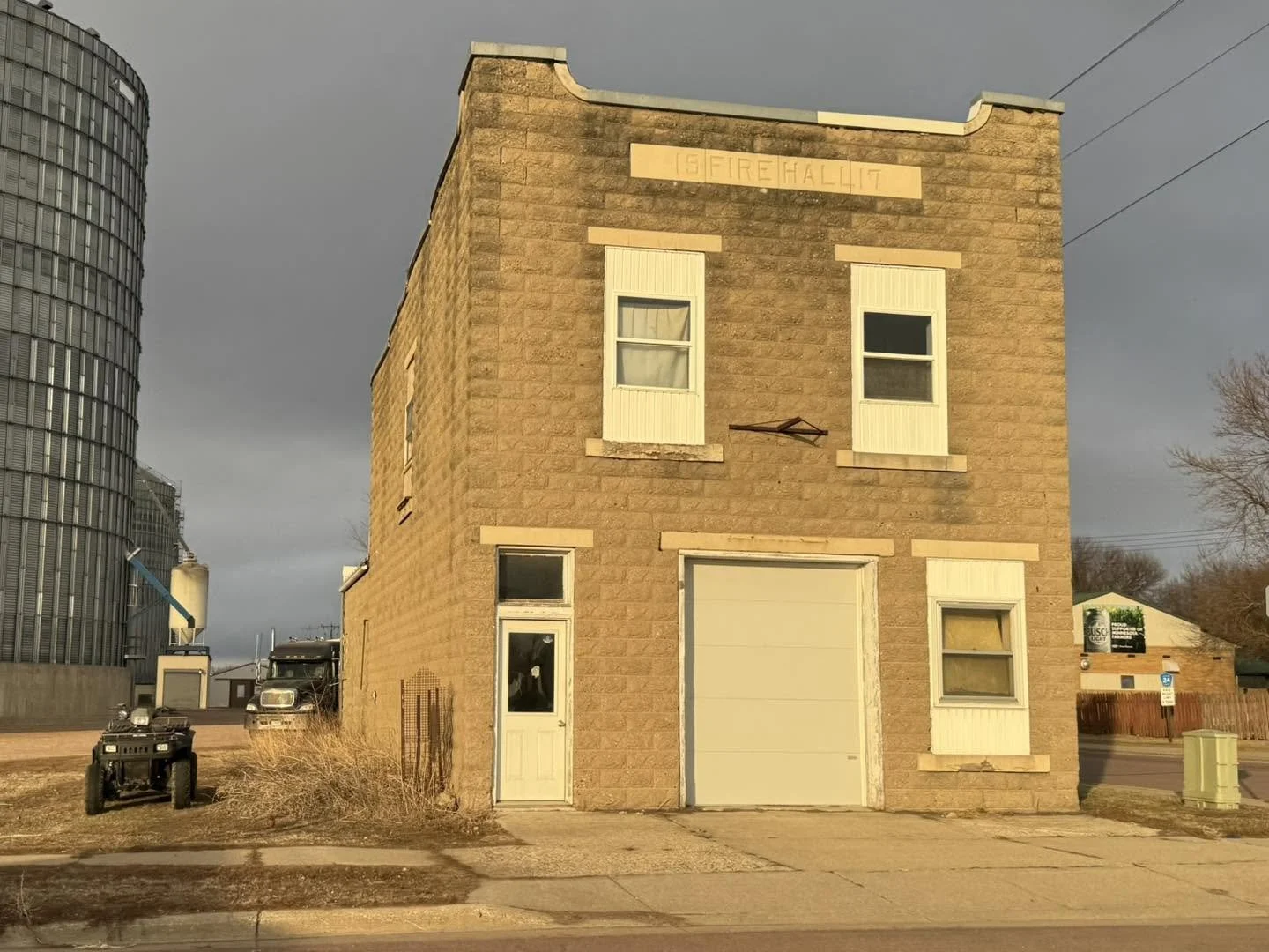 An old three-story brick building with a garage door and small windows, situated next to a modern glass building.