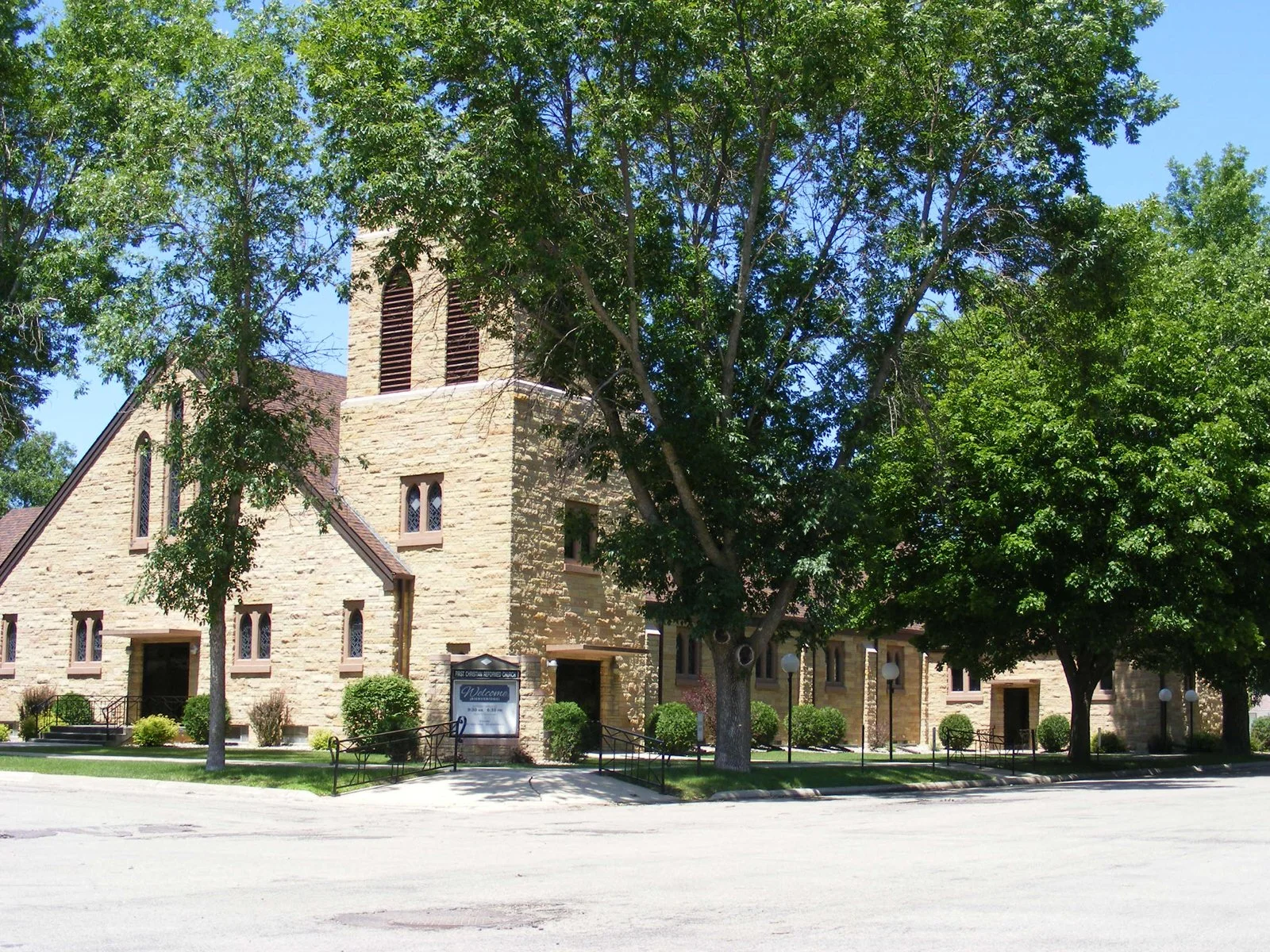 Stone church building with a tower, surrounded by green trees, under a blue sky.