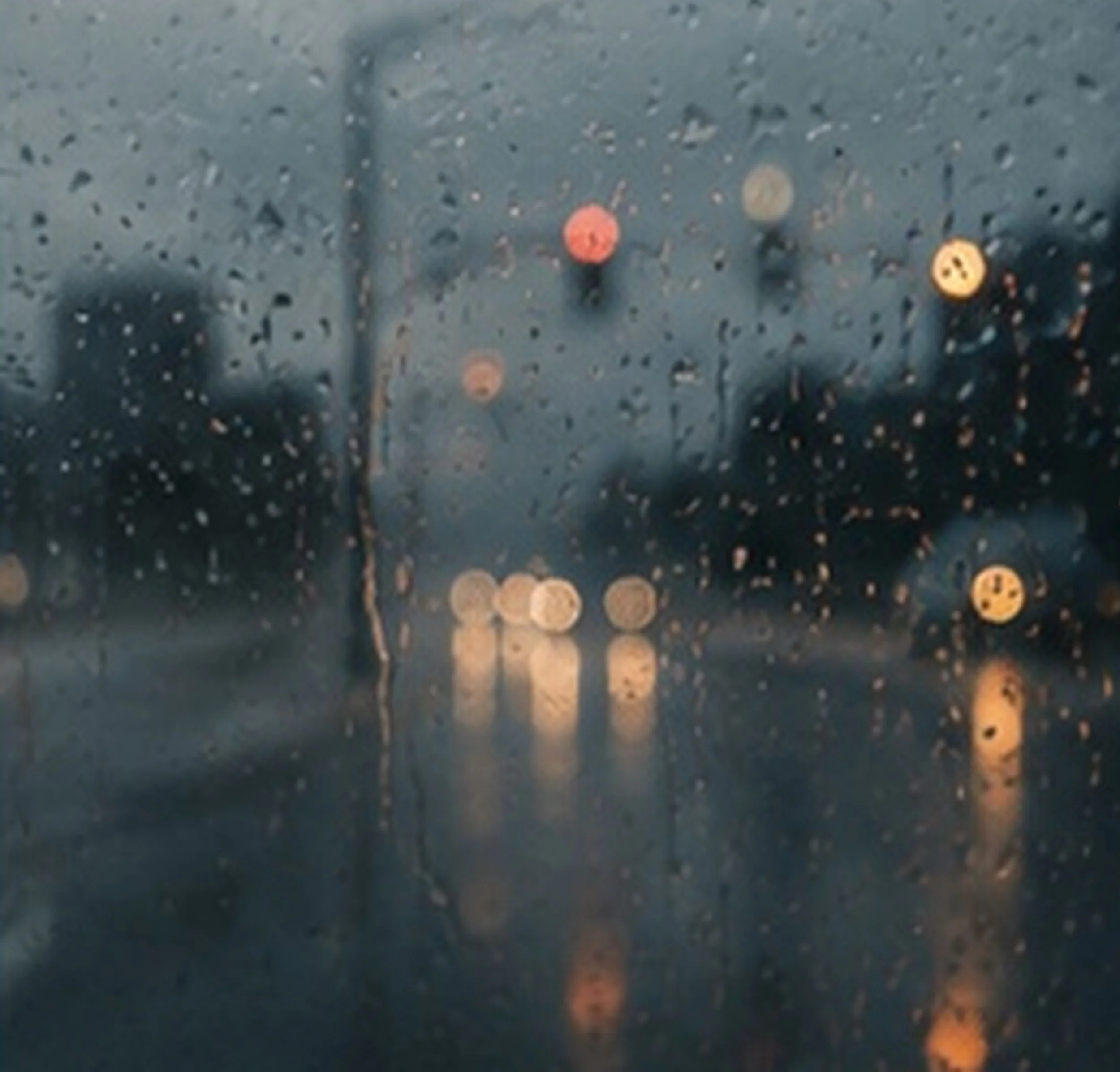 Close-up of a wet street with blurred bokeh lights in shades of yellow and red, seen through a rainy window.
