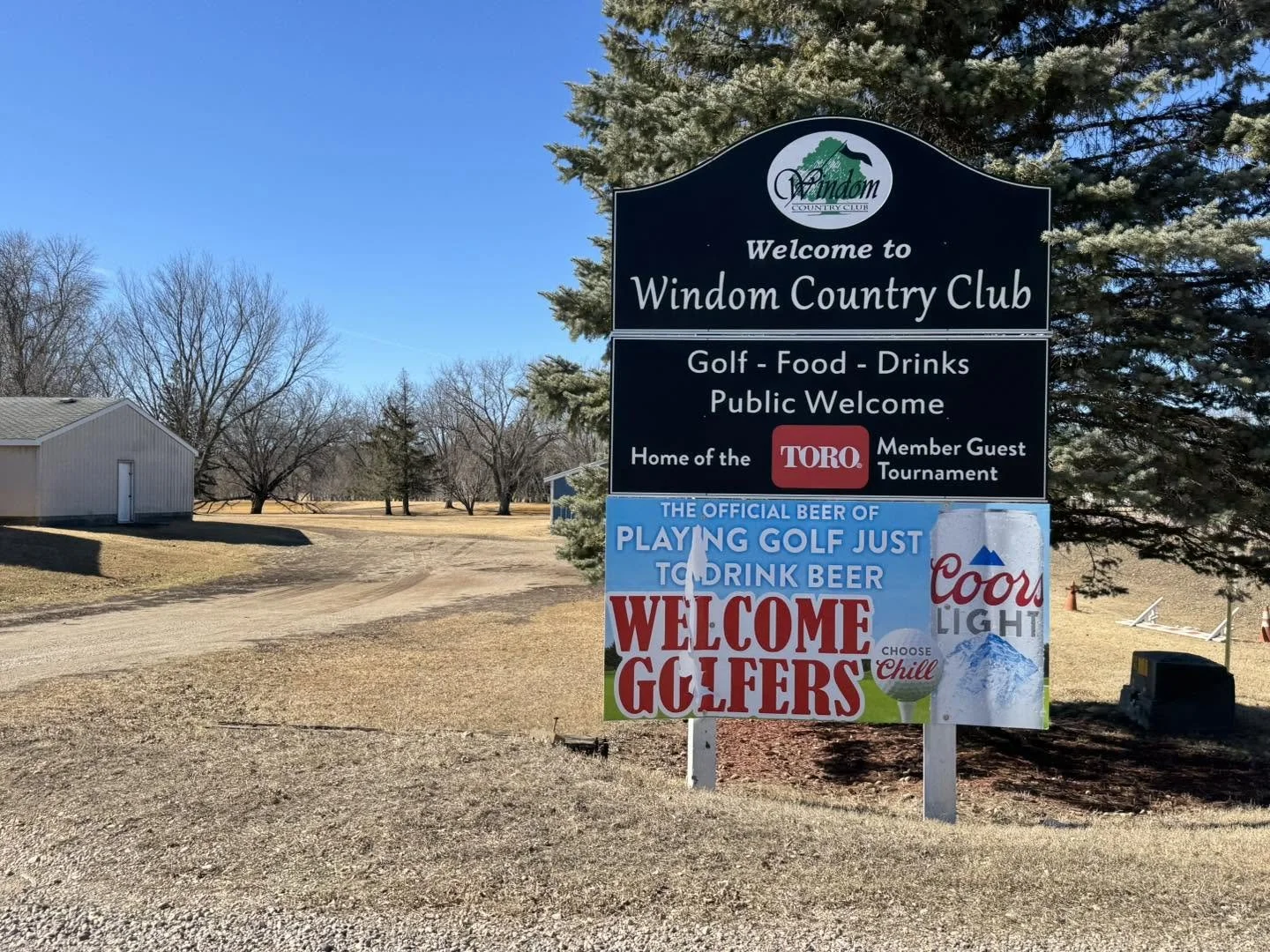 Sign at Windom Country Club welcoming visitors. It advertises golf, food, drinks, and public access. Mentions a home of Toro member guest tournament and highlights Coors Light as the official beer for playing golf and drinking beer. The sign also invites golf enthusiasts to chill.
