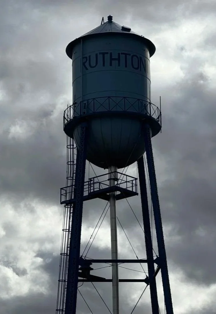 Water tower with the word 'RUTHTON' on it, standing against a cloudy sky.