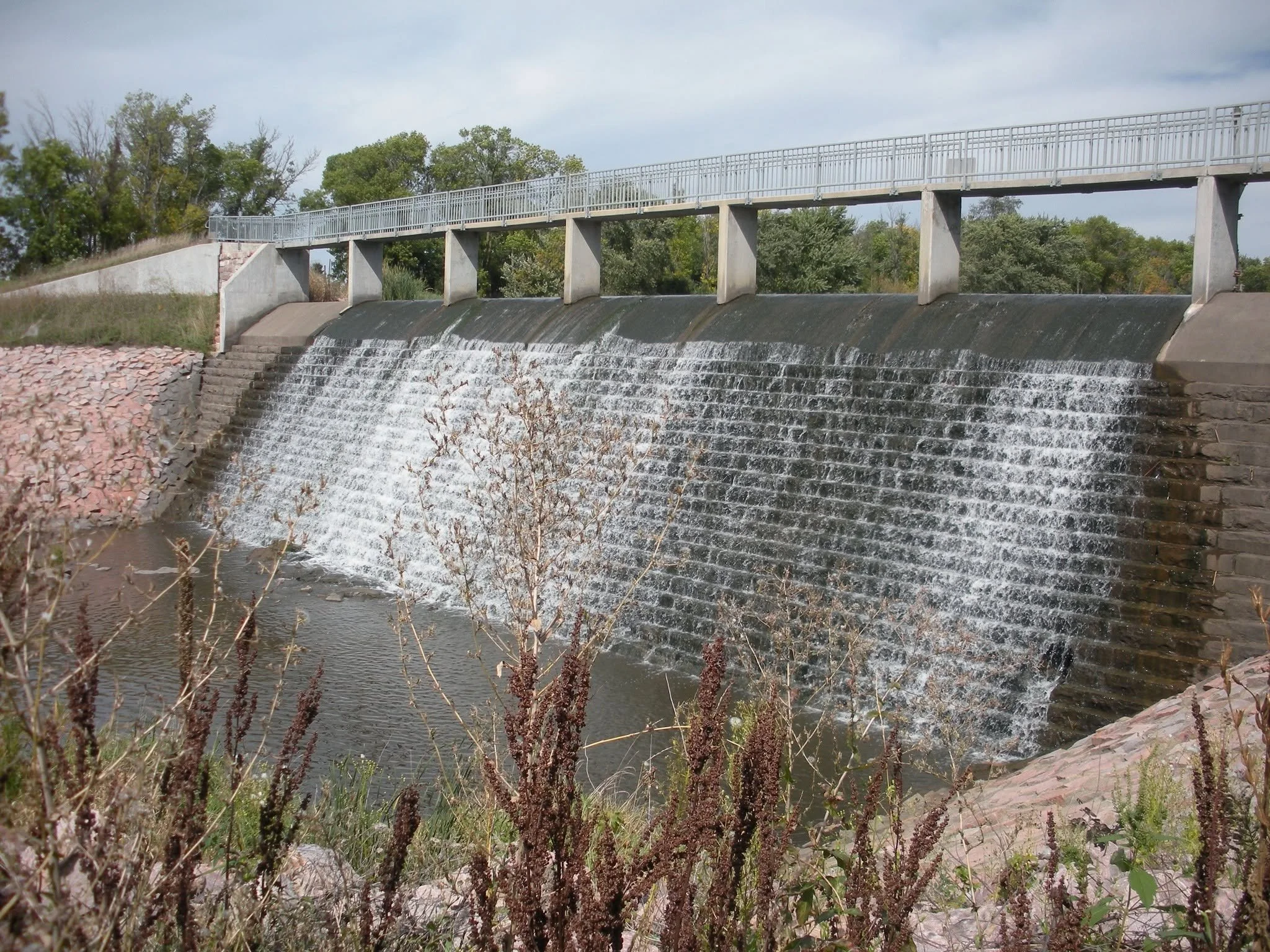 A small water dam with a metal railing and trees in the background.