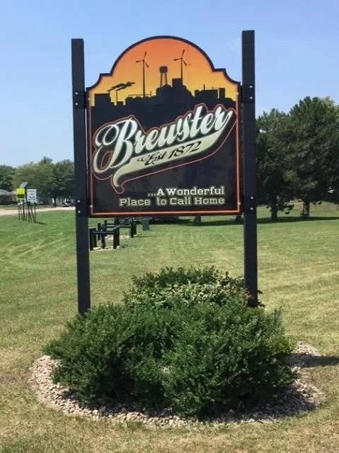Sign for Breuster, established in 1872, with the tagline "A Wonderful Place to Call Home," located in a grassy area with bushes and trees in the background.
