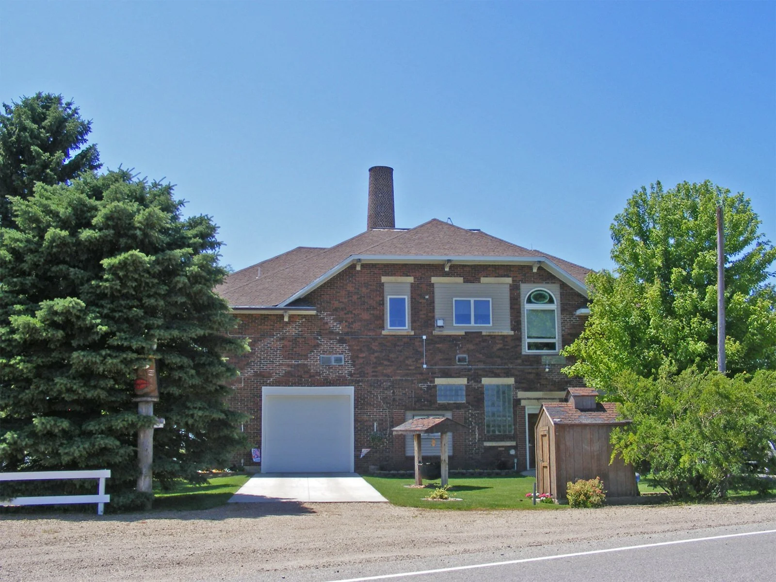 A brick house with a garage, surrounded by lush green trees under a clear blue sky.