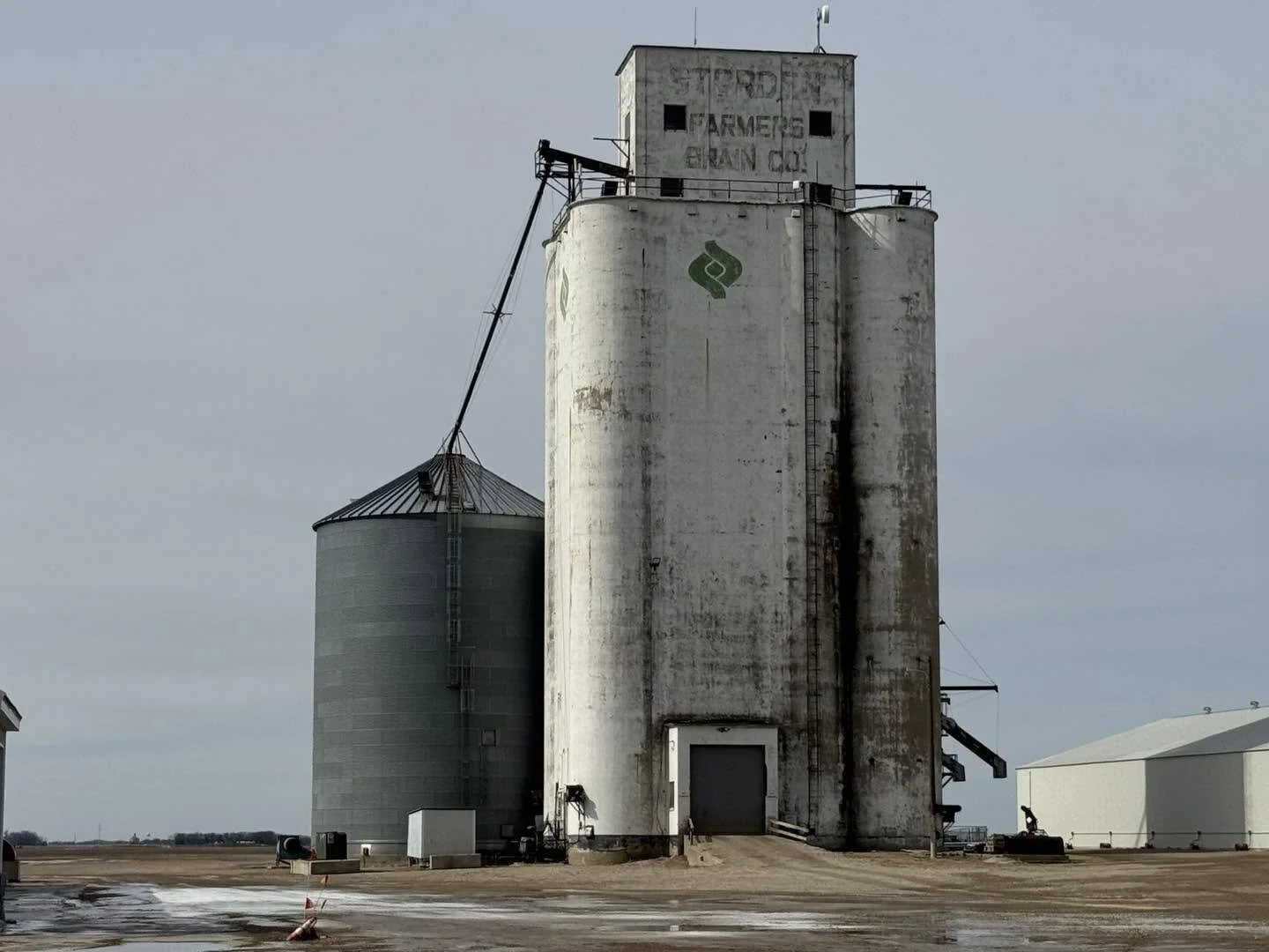 Old weathered grain silos on farmland with a cloudy sky in the background.