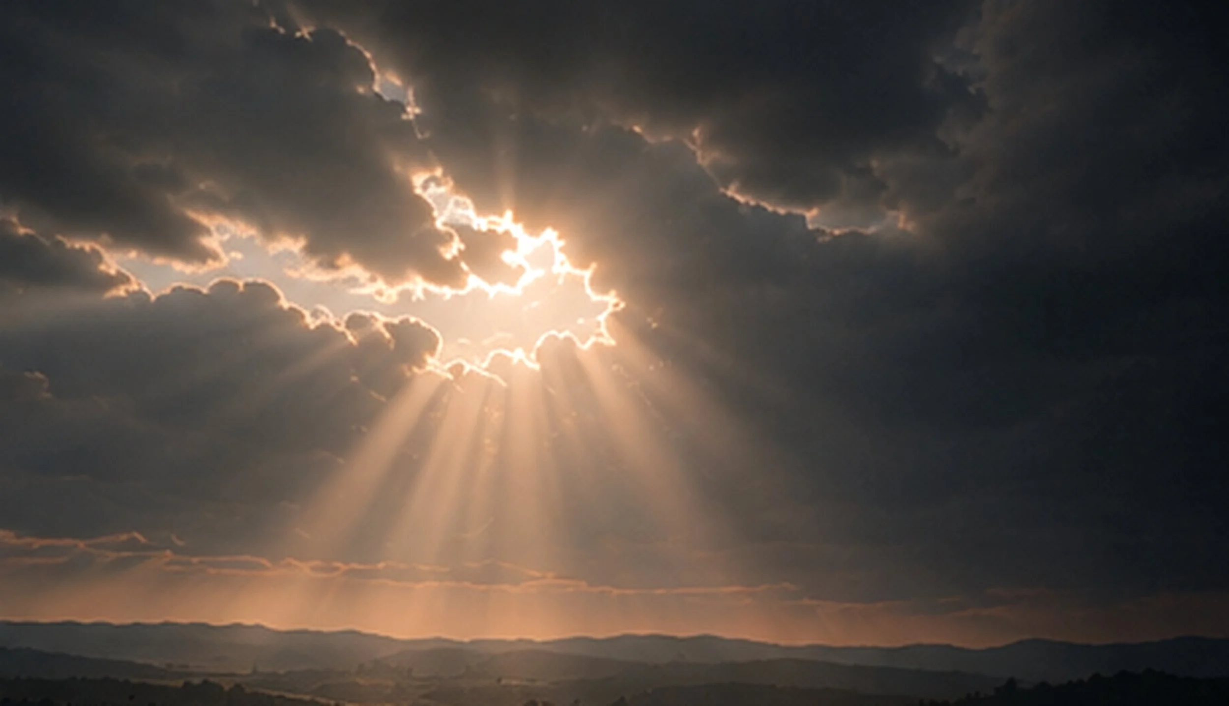 Sun rays breaking through dark clouds over a landscape.
