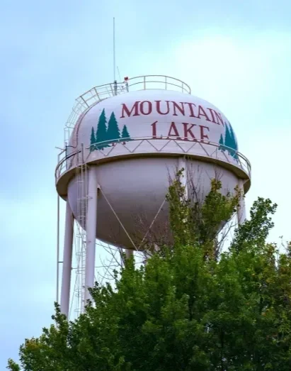 A large water tower with the words 'Mountain Lake' and pine trees painted on it, surrounded by trees.