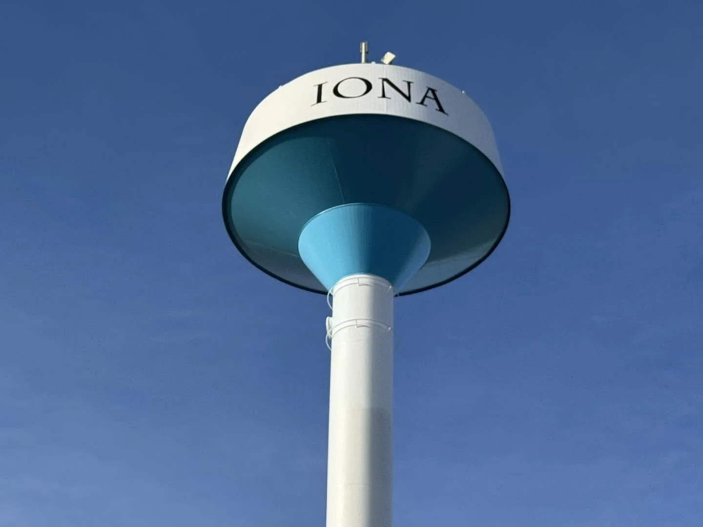 A blue and white water tower with the word 'IONA' written on it, against a clear blue sky.